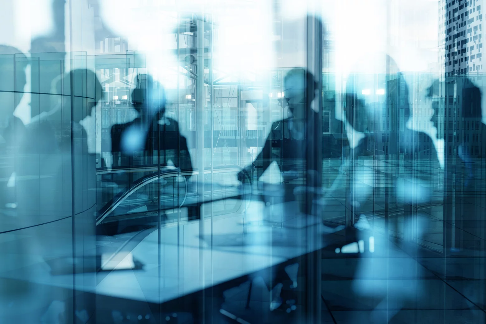 Blurred silhouettes of business people in a glass-walled office, suggesting a meeting or collaboration.